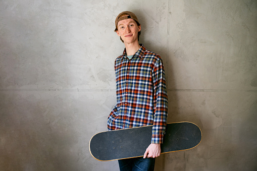 Portrait of young man, a skateboarder, against gray wall.