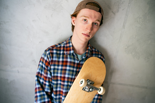 Portrait of young man, a skateboarder, against gray wall.