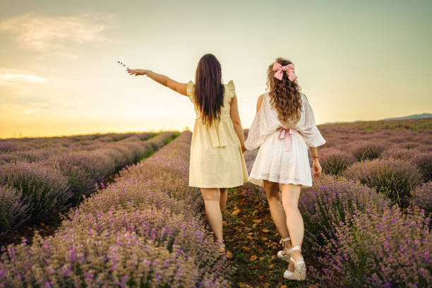 Two female friends walking through lavender field at sunset