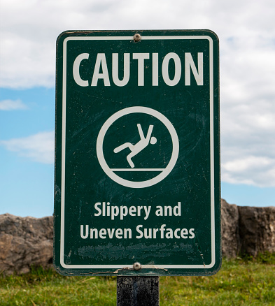A green sign cautioning about slippery and uneven surfaces, warning individuals to proceed with caution due to the potential hazards present..