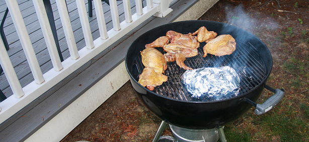 A BBQ grill with raw chicken pieces cooking on top of it. The grill bars are creating grill marks on the chicken as it cooks to perfection.
