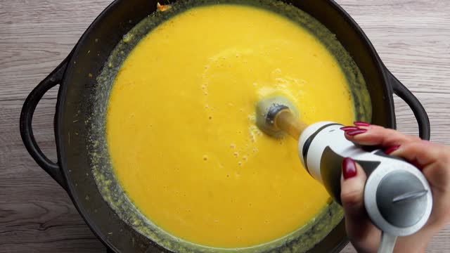 Top view of the blender mixing a pumpkin soup puree in the pan in slow motion