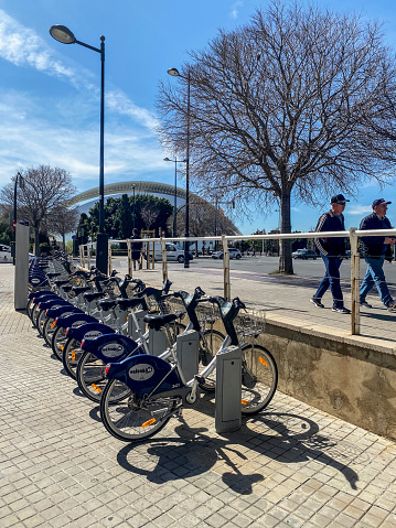 Valencia, Spain - March 13, 2024: Parked bicycles in rack in the street for public use next to the City of the Arts and the Sciences. The city government offer them for use free of charge