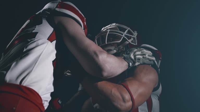 Two determined american football players in helmet training and fight in dark isolated stadium. Competitive and agressive athlete sportsmen. Usa team game, superbowl and extreme sport spirit concept.