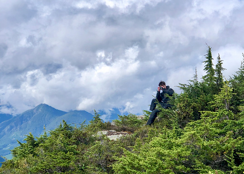 Hiker takes photo on mountain ridge, lofty clouds in distance