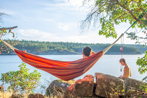 Young man relaxes in hammock above ocean, Pacific Northwest