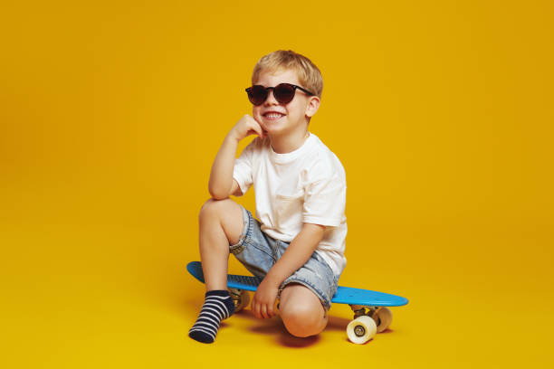 istock Cute kid in sunglasses, leaning on hand and looking at camera with smile while sitting on skateboard 2137921420