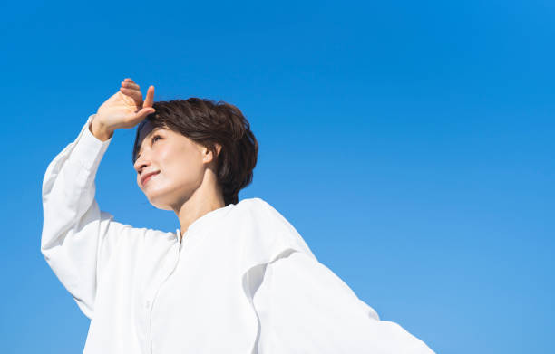 A middle-aged Japanese woman  is sunbathing.She is looking at the distant scenery.Blue sky background.