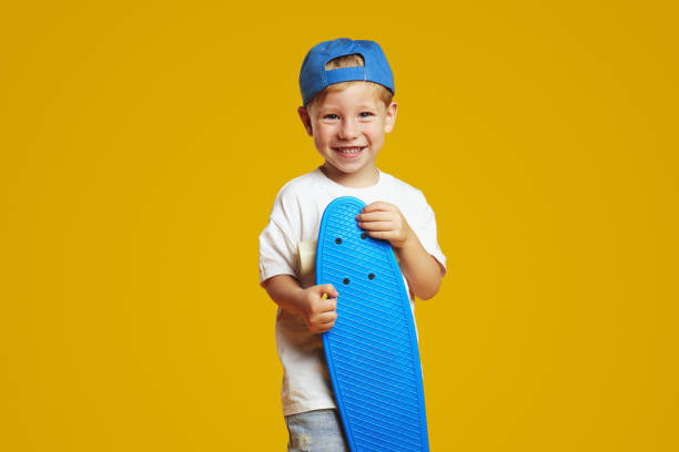 istock Funny little boy holding blue skateboard and smiling while looking at camera. 2137923565