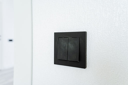 A black light switch contrasts against the white wall in a room with a television set. The rectangle display device complements the hardwood interior