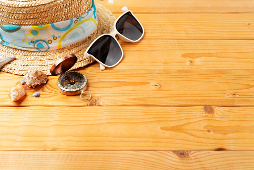 Summer holiday vacation travel planning background of straw hat, sunglasses, shells and compass on natural wooden planks