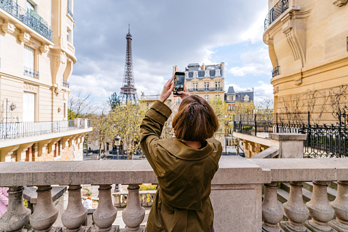 Beautiful young woman taking pictures using smart phone of an Eiffel Tower in Paris in France.