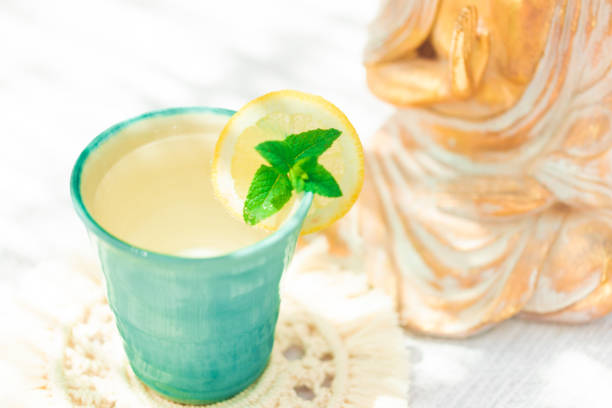 Organic lemonade in a summer turquoise Majorcan ceramic cup, with a sliced Buddha statue in the background. Some over exposing because of the sunlight.