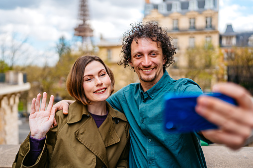 Beautiful young couple having a video call using smart phone on the street in front of an Eiffel Tower in Paris in France.