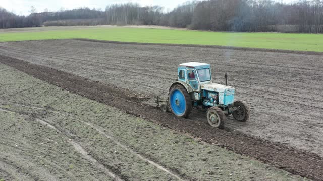 Farmer drive old rusty tractor on farmland, emit blue exhaust gas in air