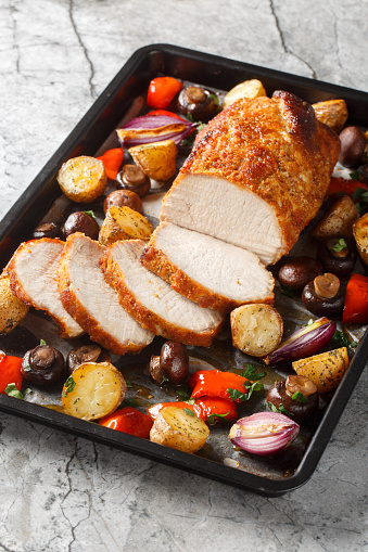 Flavor boosted pork loin baked together with potatoes, peppers, mushrooms and onions closeup on a baking sheet on the table. Vertical