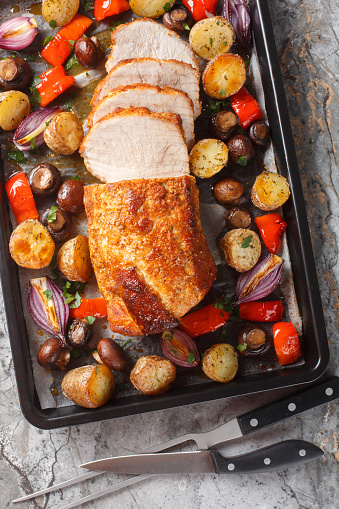 Flavor boosted pork loin baked together with potatoes, peppers, mushrooms and onions closeup on a baking sheet on the table. Vertical top view from above