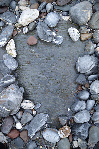 Gray white red coloured pebbles or gravel vertical photograph with variety of small and large stones  with abstract pattern making a rough rustic backdrop with one one big rock and surrounding small stones all over, copy space