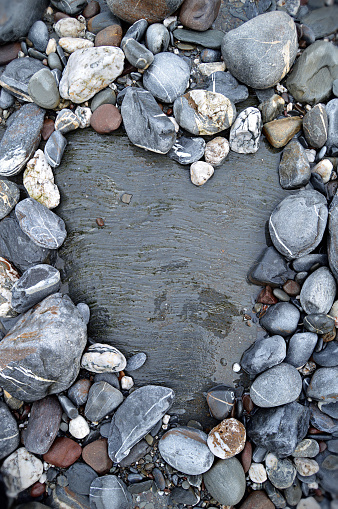 Gray white red coloured pebbles or gravel vertical photograph with variety of small large stones  with abstract pattern texture making a rough rustic backdrop with one one big textured rock in heart shape with surrounding small stones all over, copy space