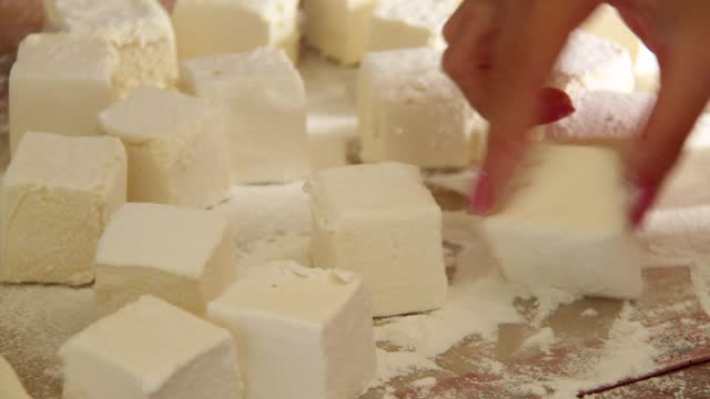 Woman's hand rolls marshmallows dessert in powdered sugar.