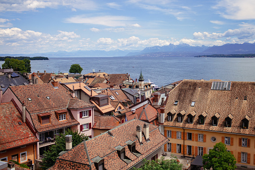 Panoramic view of Nyon terracotta rooftops with Lake Geneva and the Alps in the distance, embodying tranquility.