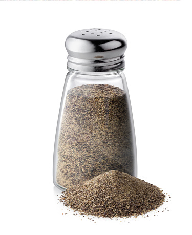 Pepper shaker with pile of ground black pepper isolated on white background.