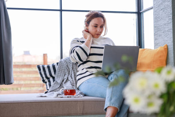 istock Young woman using a laptop computer while relaxing on the windowsill sofa at home 2138131506