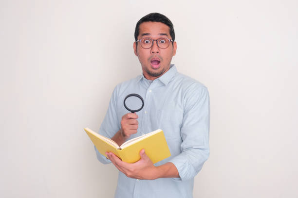 A man showing shocked face while holding magnifying glass and book