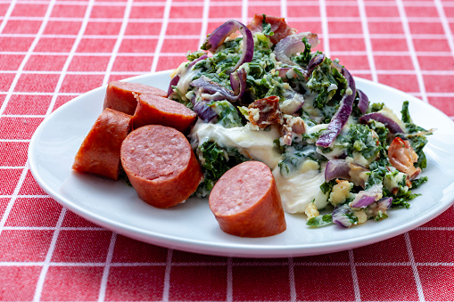 Boerenkool met worst is a traditional Dutch dish with mashed potatoes, kale, smoked sausage, Spanish onions and melted cheese. Studio shot.