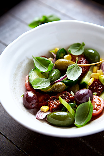 Simple Salad with Green and Kalamata Olives, Cucumber, Cherry and marinated Tomatoes, Capers and Jalapeno Pepper. Brown wooden background.