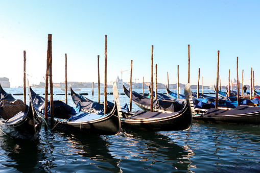Traditional Venetian gondolas moored and docked by wooden poles on the Venetian lagoon by Riva Degli Schiavoni, the monumental waterfront of Venice, Italy