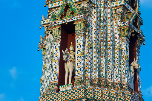 Detail of the small Prang, the side tower of the Wat Arun (Temple of Dawn) in Bangkok, Thailand, wind god Vayu on horseback against blue sky. Encrusted with coloured faience