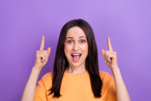 Photo of astonished woman dressed orange t-shirt indicating at impressive discount empty space isolated on purple color background.