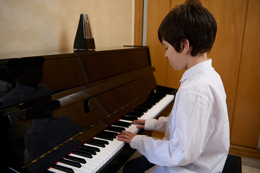 Confident portrait of an elementary age preteen boy, talented musician pianist sitting at grand piano, enjoys the rhythm of classical music while plays piano. Hobbies and leisure. Music lesson