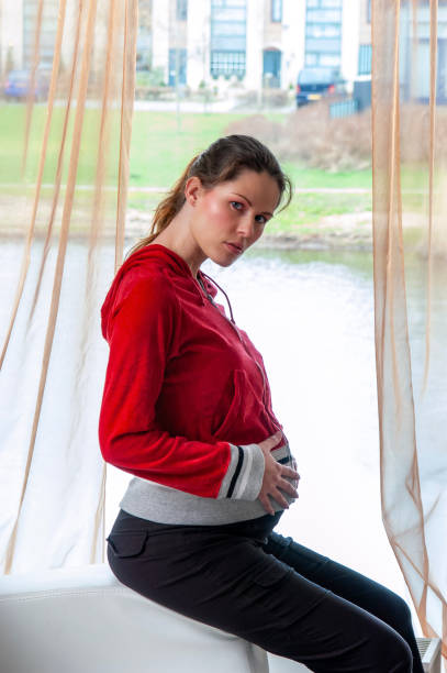 Young pregnant woman, sitting on coach hands on her back. suffering from backache. Looking at camera.