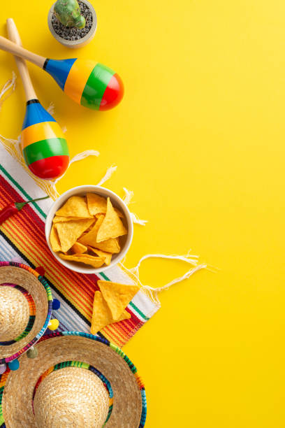 istock Cinco de Mayo decorative setting. Look from vertical top view at traditional symbols: party sombreros, maracas, cactus in flowerpot, serape, nachos in serving bowl on a yellow canvas, space for text 2138301578