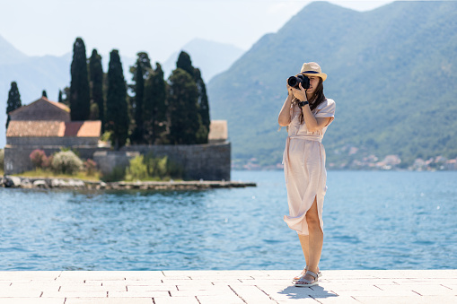 Young travel lady in dress takes photo with professional camera at sunny day. Young female photographer at her vacation trip in europe