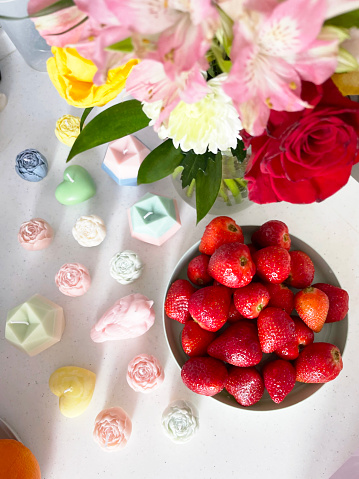 beautiful aesthetic background. top view of candle figures, a plate of strawberries and a bouquet of flowers