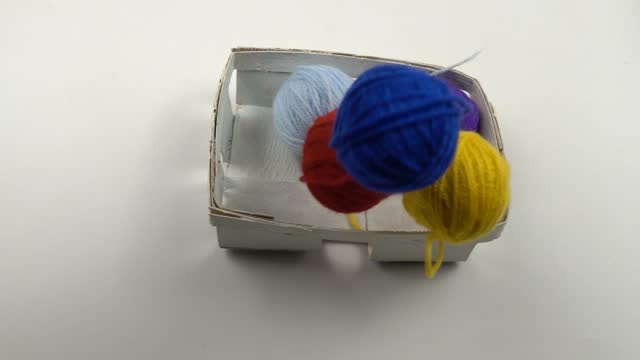 Colorful balls of threads for hand knitting falling into the white small basket, slow motion