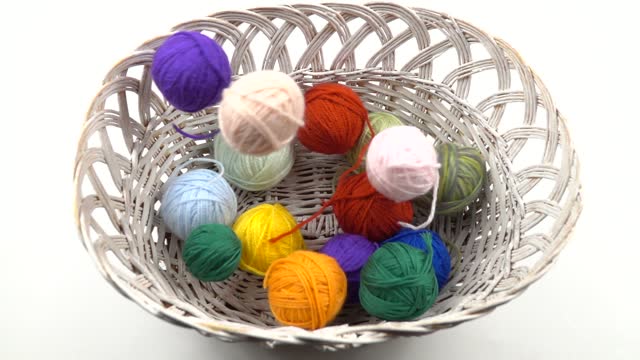 Colorful balls of threads for hand knitting falling into the white wicker basket, slow motion