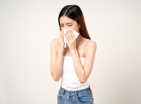 Suffering from runny nose and high temperature. Cold and fever concept. Portrait of beautiful young asian sick woman over isolated white background being wrapped in scarf sneezing.