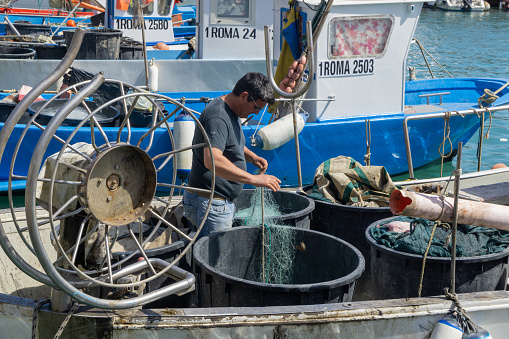 A fisherman is working on fishing nets on his boat in the port of Anzio, Rome, Italy