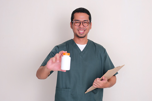 A male nurse smiling while holding medicine bottle and a clipboard