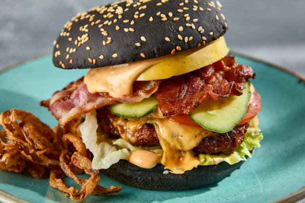 istock Gourmet black burger with bacon and crispy onions on a turquoise plate, gray textured backdrop with a hint of sunlight 2138424462