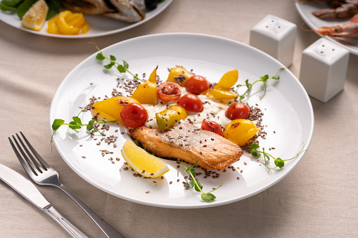 Baked salmon served with tomatoes grill, lemon and microgreen on white plate. Copy space