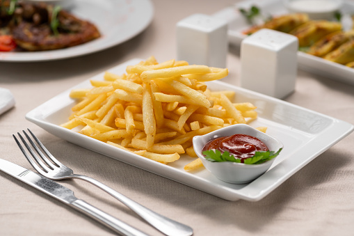Fried French fries served on a white plate with ketchup in a restaurant. Fast food cafe menu. Copy space