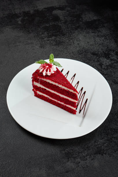 istock Red velvet cake on white plate on dark stone background. Popular red cake with layer biscuit and cream. Red velvet dessert in minimal style on black backdrop. Piece of cake with mint. 2138440578