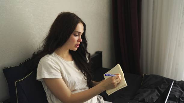 istock Young woman writing notes while working with laptop at home 2138480166