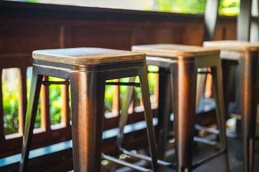 Row of tall wooden and iron retro style seats at the coffee counter bar. Furniture object photo, close-up and selective focus at the seat's part.