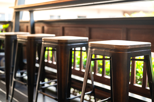 Row of tall wooden and iron retro style seats at the coffee counter bar. Furniture object photo, close-up and selective focus at the seat's part.